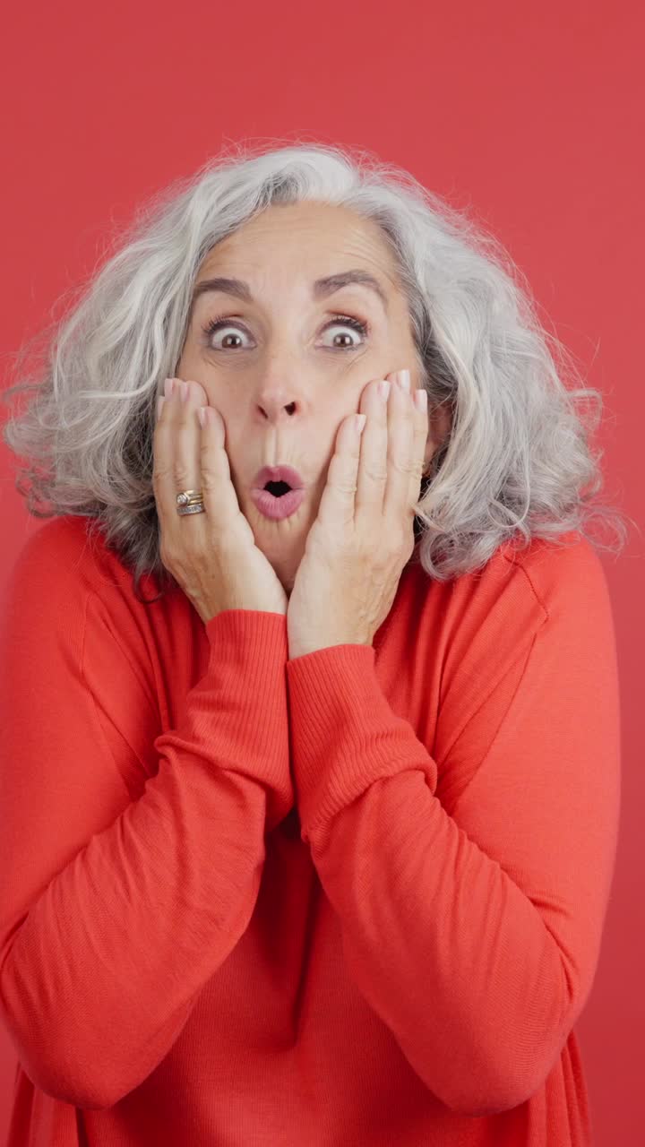 Surprised older woman expressing shock against a red background