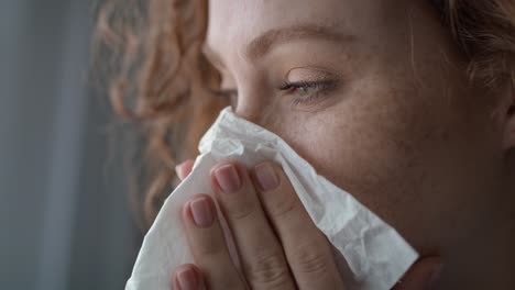 Close-up-of-young-caucasian--red-head-woman-sneezing-and-blowing-nose-into-tissue-at-home