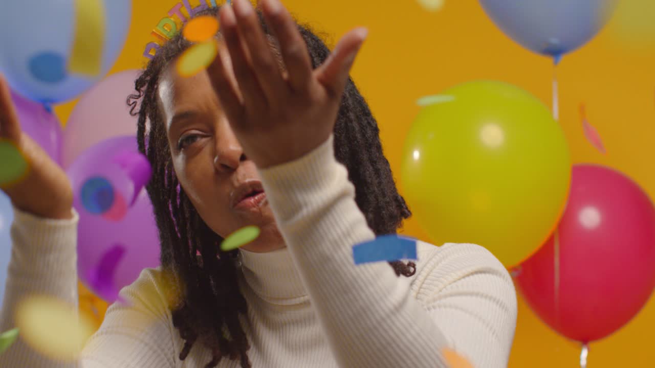 retrato de estudio de una mujer con una cinta para la cabeza de cumpleaños celebrando soplando confeti de fiesta de papel 1