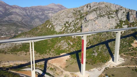 aerial shot of the fully finished moracica bridge in montenegro. the big red coat of arms of montenegro is seen on one of the bridge's pillar