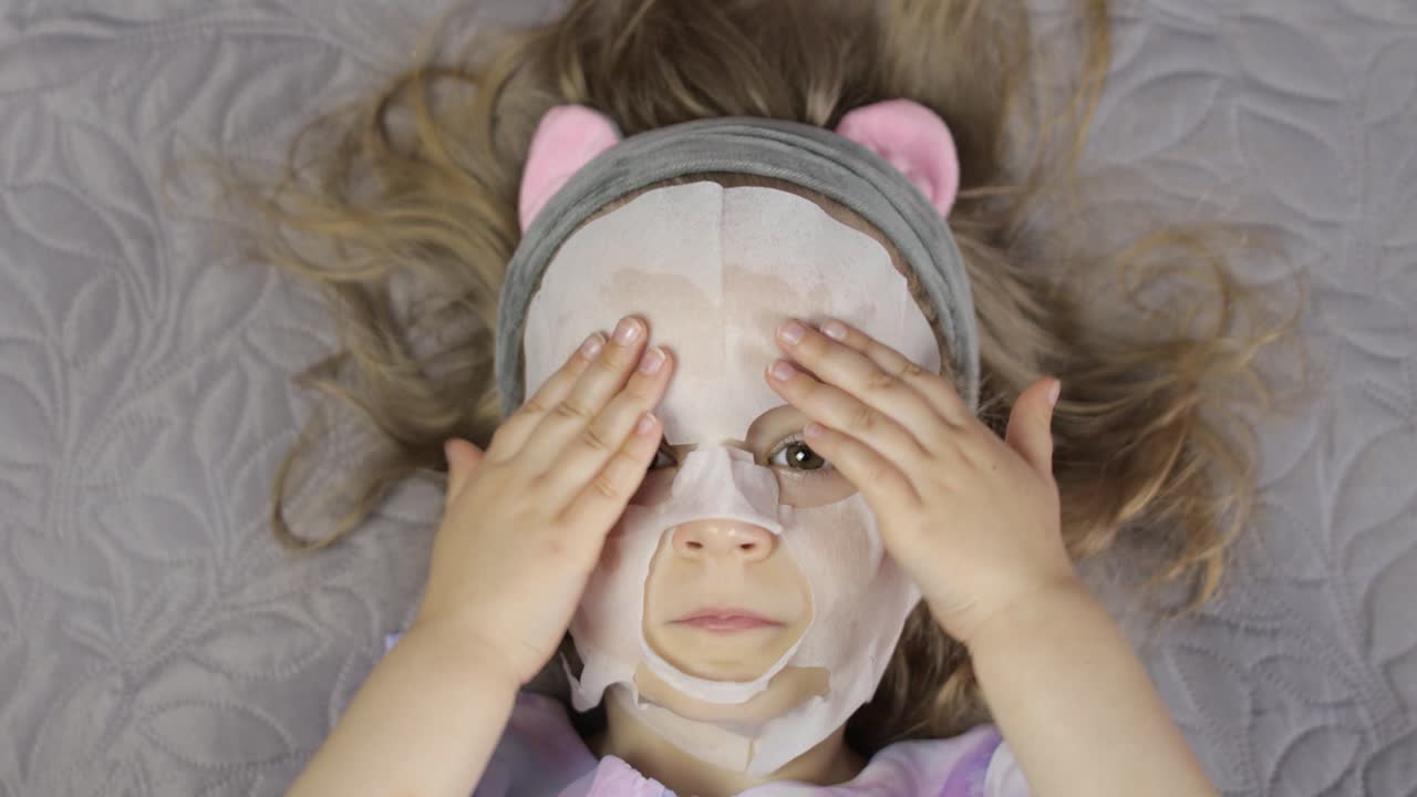 Teen girl applying moisturizing face mask. Child kid take care of skin with cosmetic facial mask