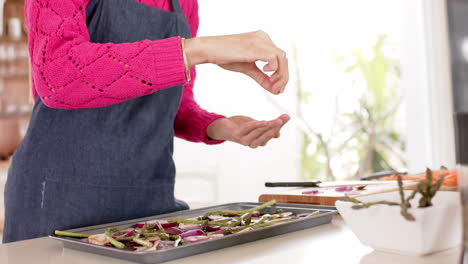 Mid-section-of-biracial-woman-preparing-food-in-kitchen-at-home-with-copy-space,-slow-motion