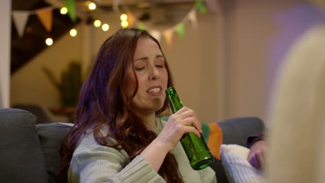 relaxed group of friends sitting on sofa at home or in bar celebrating st patrick's day with party drinking alcohol