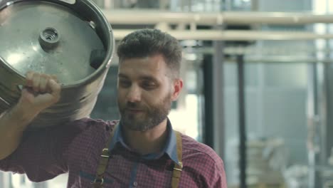 joven cervecero con un delantal de cuero sostiene un barril con cerveza artesanal en una cervecería moderna