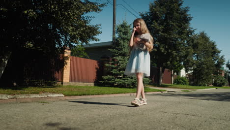 young girl wearing light blue dress stands alone on quiet suburban street, holding soft bunny toy in hands while rubbing eyes under sunlight with tree and fence shadows cast on pavement