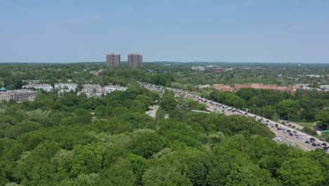 an aerial view over a large park with green trees, next to a busy parkway