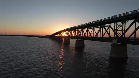 aerial: pulling back from an old broken down bridge at sunset over the ocean