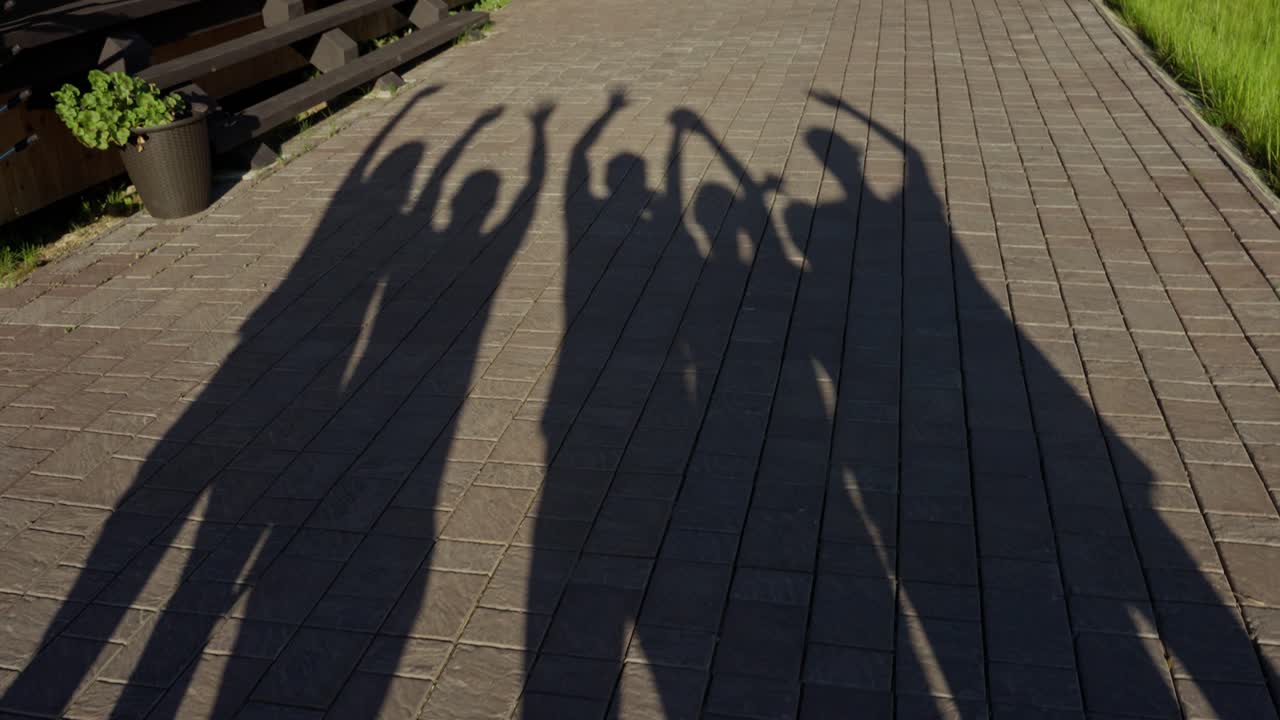 Shadows of people with arms raised on a path