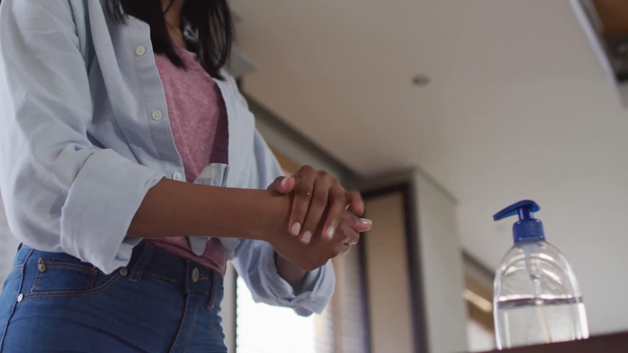 mujer de raza mixta con máscara en casa desinfectando las manos