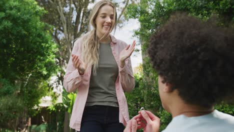 Happy-diverse-couple-proposing-and-smiling-in-garden-on-sunny-day