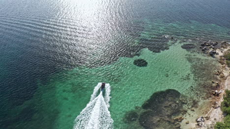 a speedboat cruises on turquoise waters along the rocky coastline of sardinia