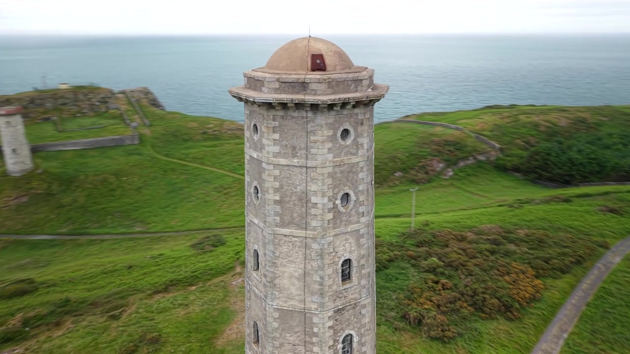 İrlanda'nın Wicklow Head kıyı şeridinde tarihi deniz feneri kulesinin drone ile yakın çekim dönme görüntüsü.