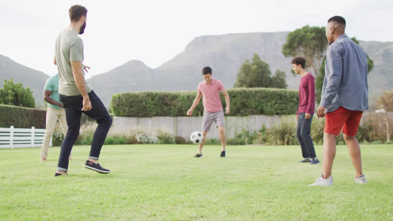 행복한 다양한 남성 친구들이  ⁇ 은 날 정원에서 축구를 하고 있습니다.