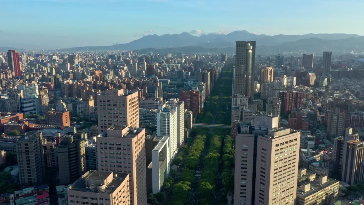 고층 건물로 둘러싸인 나무와 배경에 있는 산의 실루엣이 있는 녹색의 유명한 레나이 도로를 통해 느린 공중 전진 비행