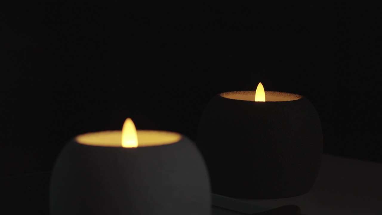 Due candele a LED su sfondo nero, corpo bianco e scuro rotondo con luce pulsante