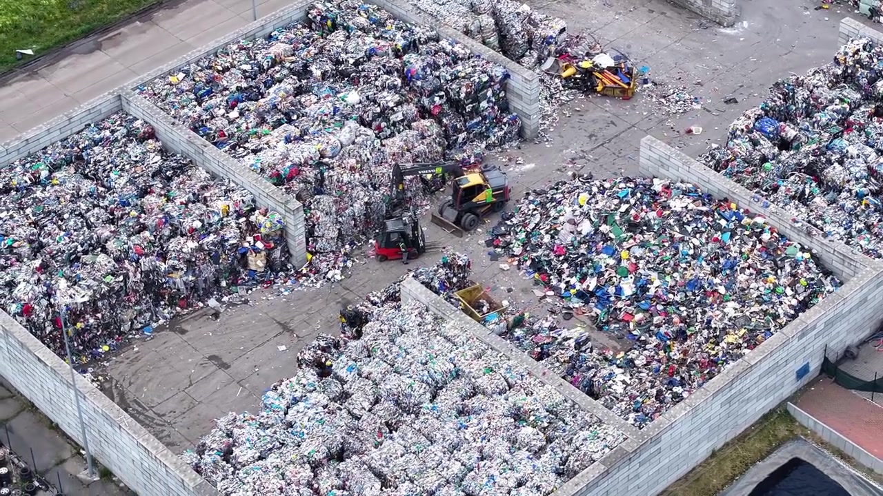 Processes plastic waste at a recycling facility. Forklifts move materials. Large piles of sorted waste sit in separate areas. Facility focuses on waste management solutions.