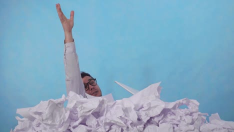 perplexed man office worker with a laptop in a large heaps of crumpled paper on a blue background