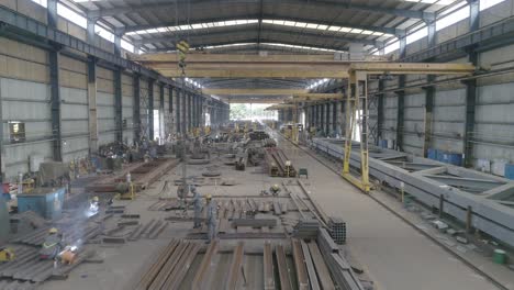 drone view of workers and equipment in a steel fabrication warehouse building.