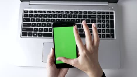 female hands doing pinch to zoom on the smartphone's touchscreen. green screen, chromakey concept, laptop in the background. top shot 60 fps