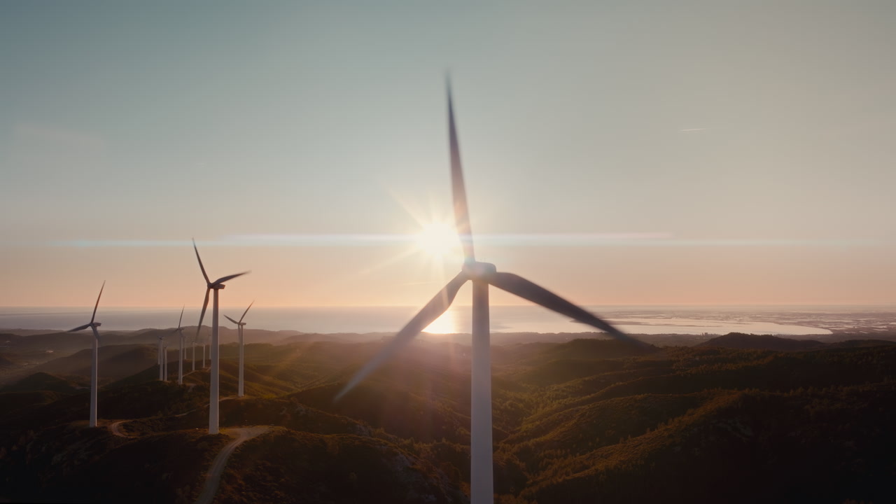 Cinematic 4K aerial drone footage of wind turbines at sunset over coastal hills. Clean renewable energy, sustainable power generation, green technology and climate friendly infrastructure.