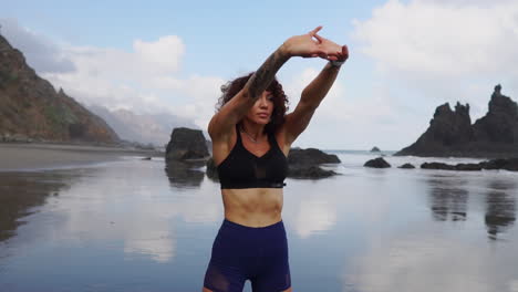 junto al océano, una mujer joven practica estiramiento y yoga mientras mira a la distancia, como se ve en cámara lenta