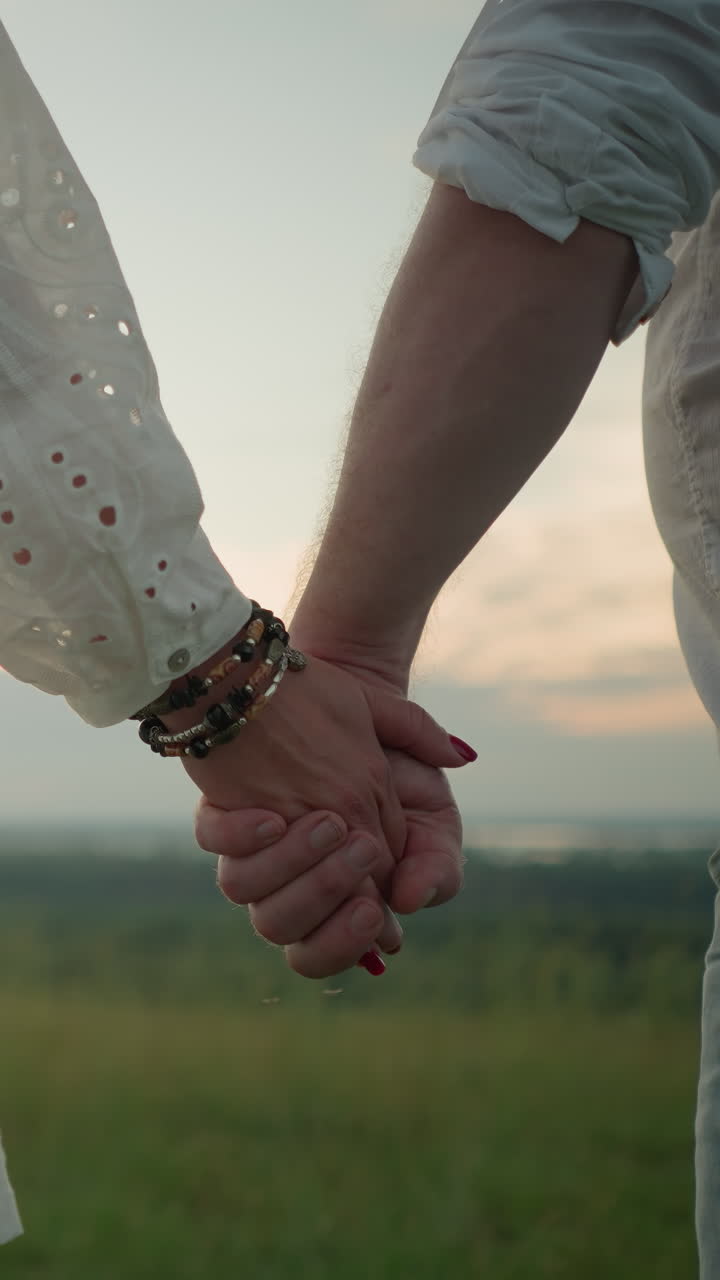 un primer plano de dos manos que se sostienen suavemente, con la mano de la mujer adornada con pulseras de cuentas y uñas rojas. la suave luz del sol se filtra en el fondo