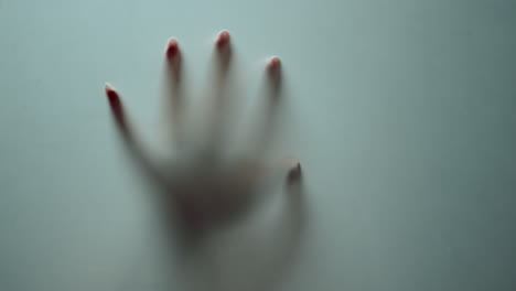 Macro-female-hand-shadow-sliding-down-on-glass-surface.-Mystical-horror.