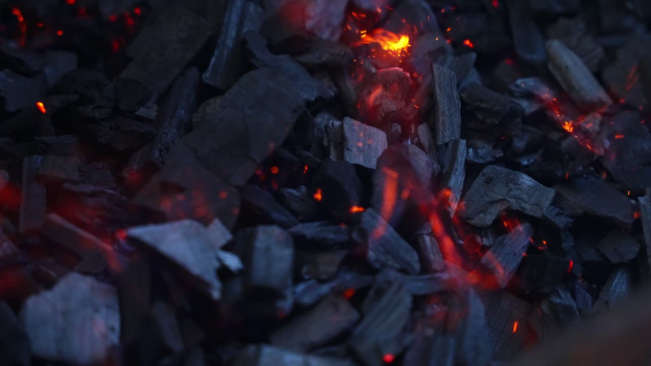 Glowing charcoal embers and ash with sparks heat shimmering, smoke floats in slow motion