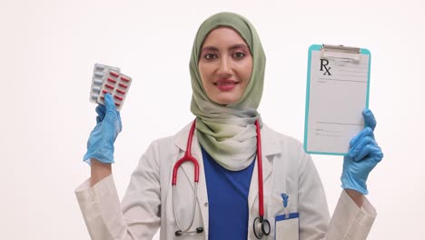 a female doctor in a hijab holding a prescription pad and a blister pack of pills