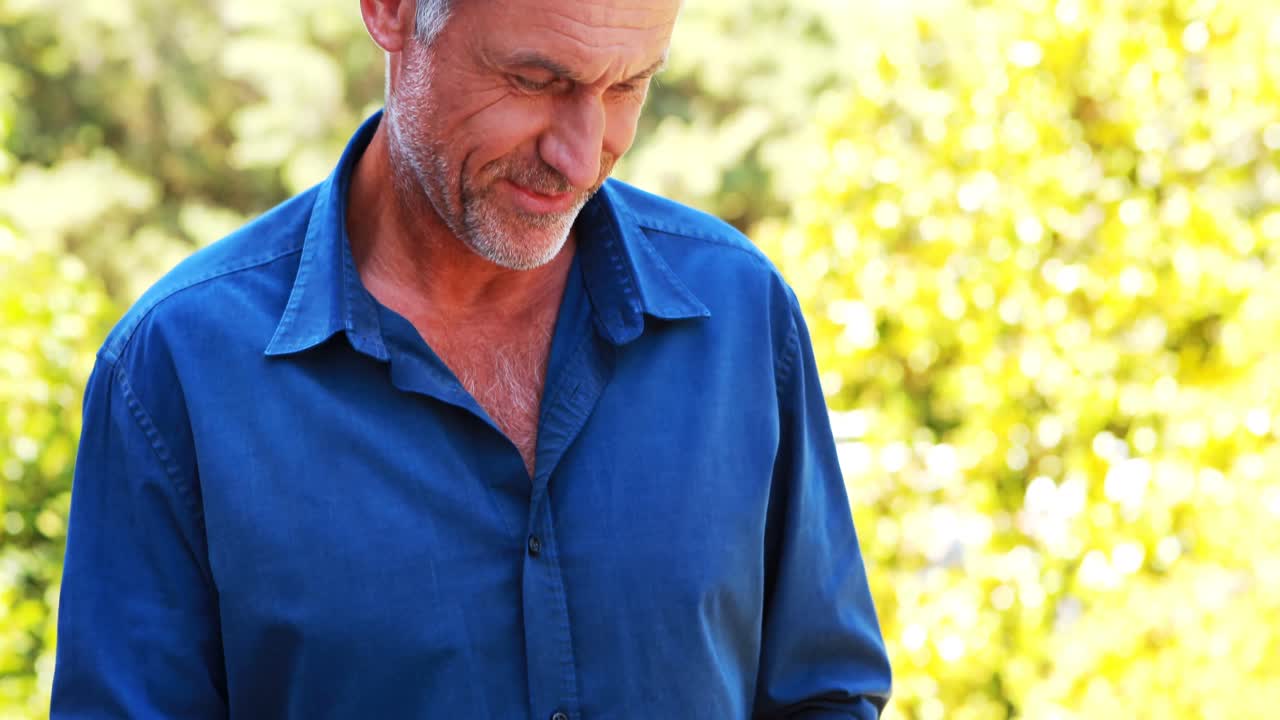 Uomo maturo sorridente che usa un tablet sul balcone.