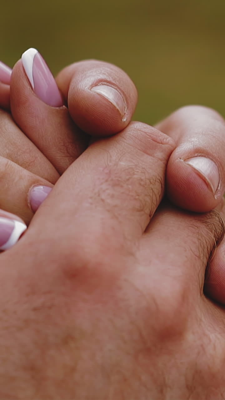 CU, slow motion: careful man wearing elegant suit holds hands of future wife in beautiful white dress at bust on green background extreme closeup