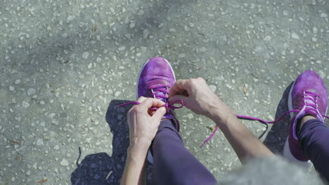 middle-aged female legs and hands tying laces on running shoe