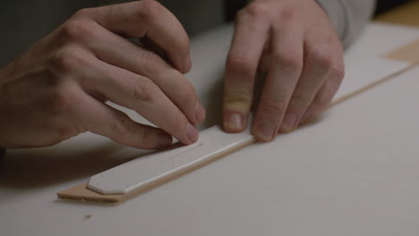 Close-up of hands precisely positioning a template on a leather piece for crafting, focusing on accuracy.