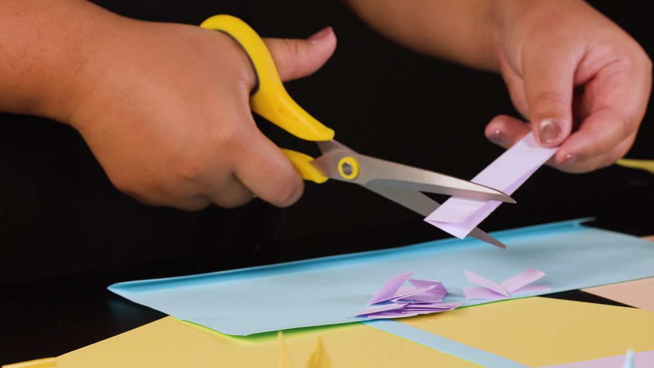 Primo piano di mani che usano forbici gialle per tagliare strisce di carta viola su carta blu