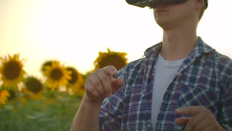 a student in plaid shirt and jeans uses vr glasses on the field with sunflowers for scientific article. these are modern technologies in summer evening.