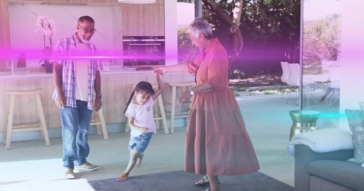 Nonna che offre la mano alla nipote che gira sul tappeto, mentre il nonno applaude celebrando la vita familiare.