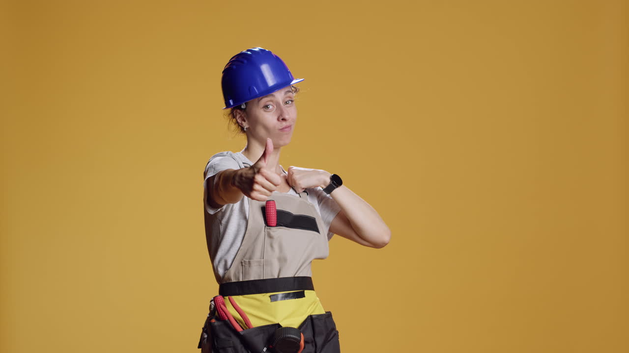 Portrait of female construction worker giving thumbs up in studio