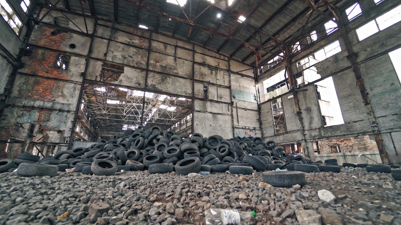 Big old empty factory with garbage and a pile of used rubber tyres inside. Tires that are no longer suitable for use on vehicles in a damaged plant.