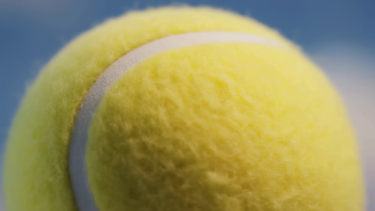 Tennis ball showing visible action, in sky background, with tennis ball, from a close-up perspective, with yellow, white accents, and neutral mood, showing nearby objects and surrounding setting.