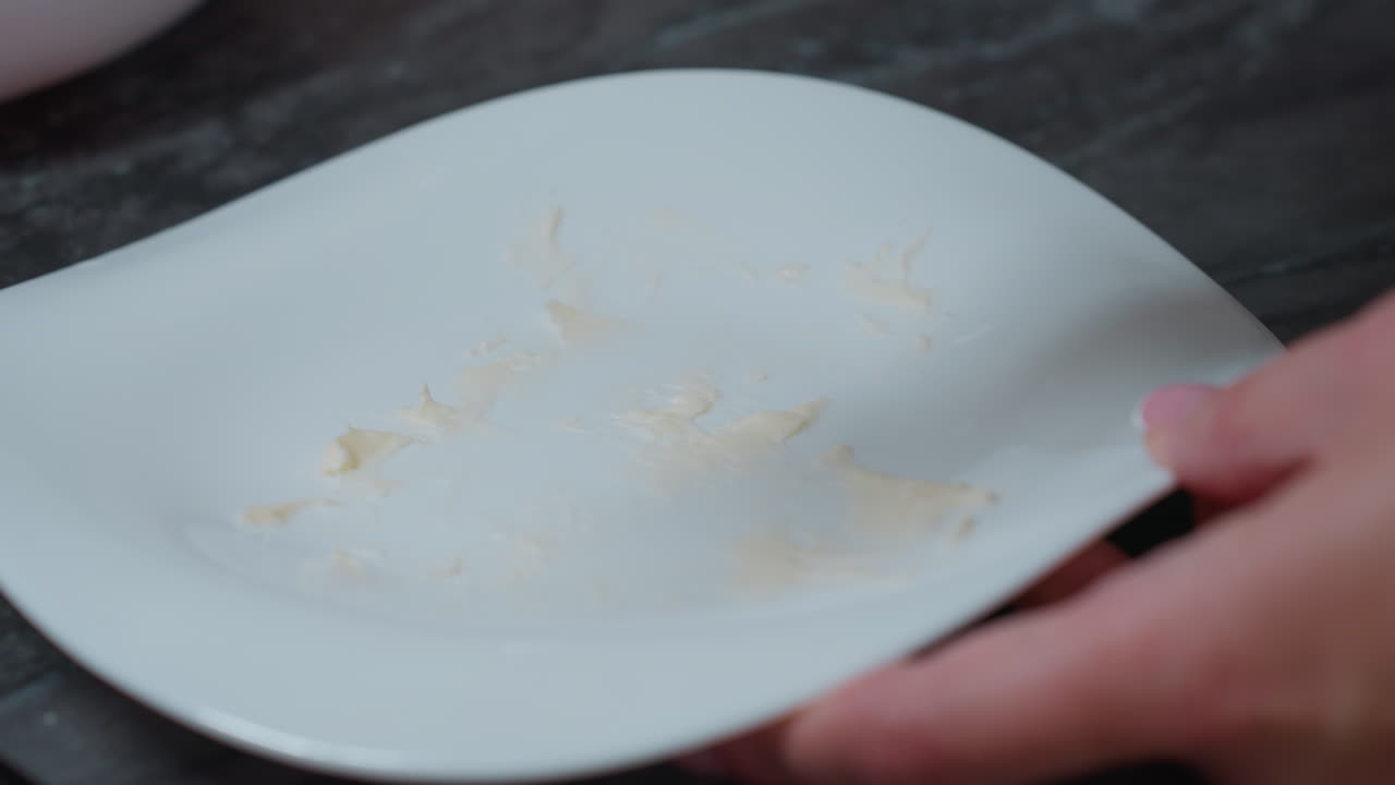 백색 접시 위에 칼로 조심스럽게 잘라지는  버터의 클로즈업, 부드러운 버터의 질감이 부의 배경과 대조되어 깨하고 미니멀한 환경을 보여줍니다.