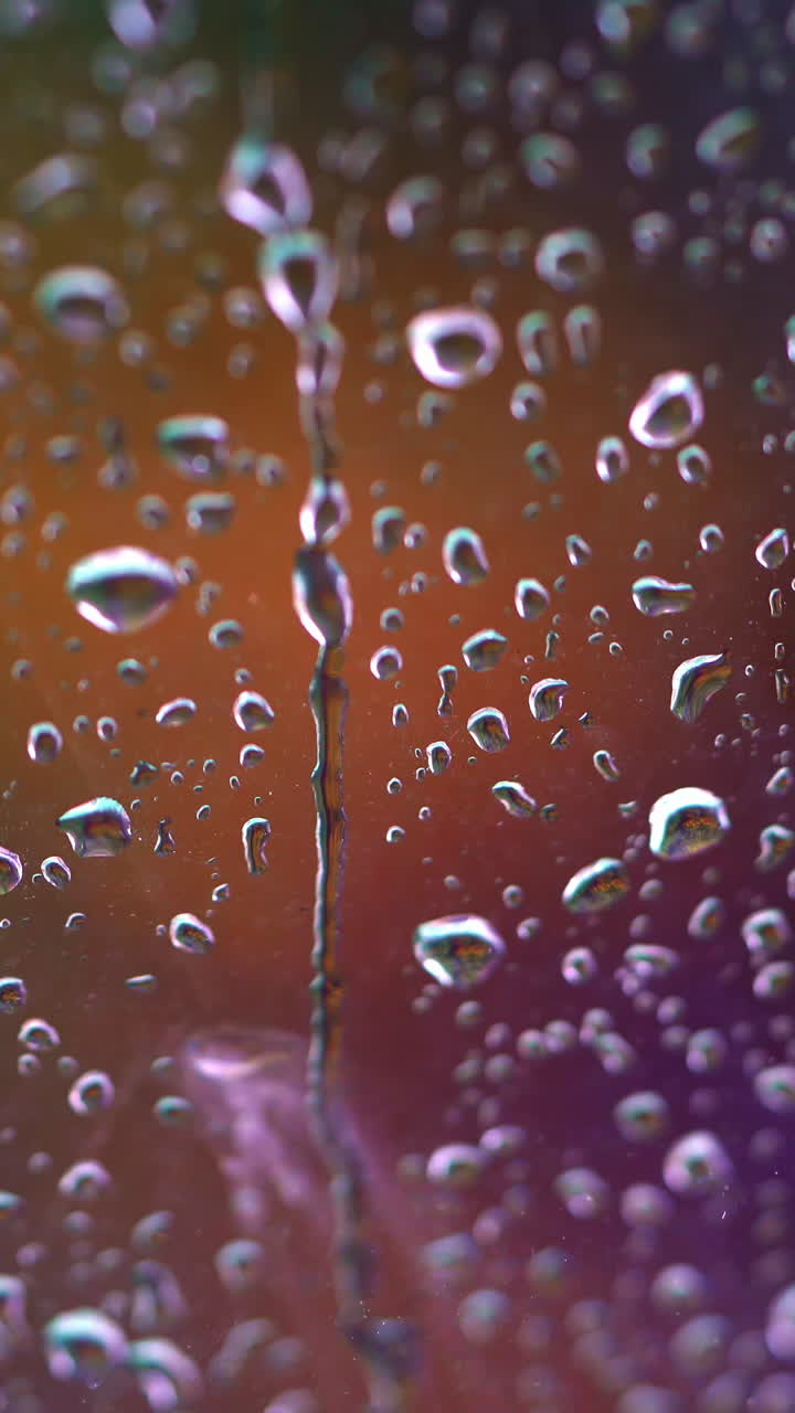 Droplets on colorful background. Raindrops flow down the glass window. Drops of water falls into the window. Close-up. Vertical video