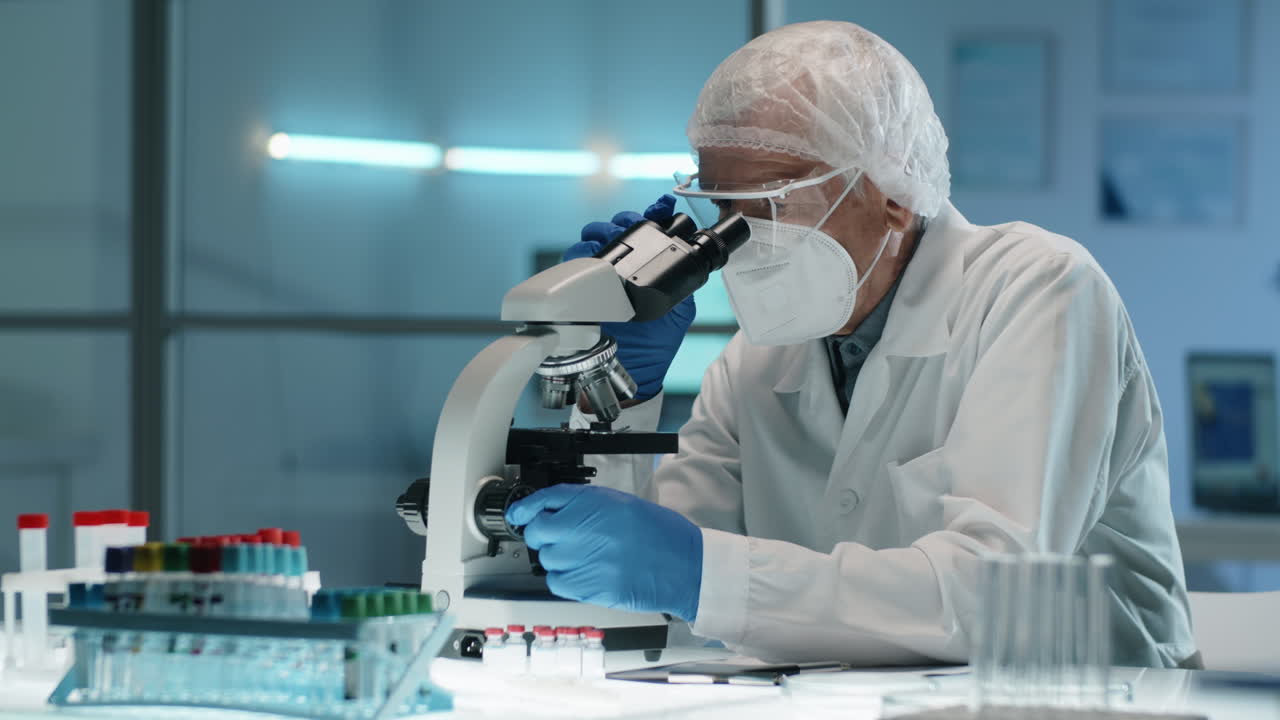 Elderly Scientist in Protective Uniform Using Microscope