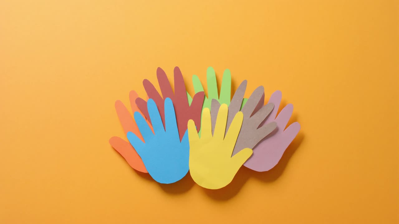 Close up of hands together made of colourful paper on orange background with copy space