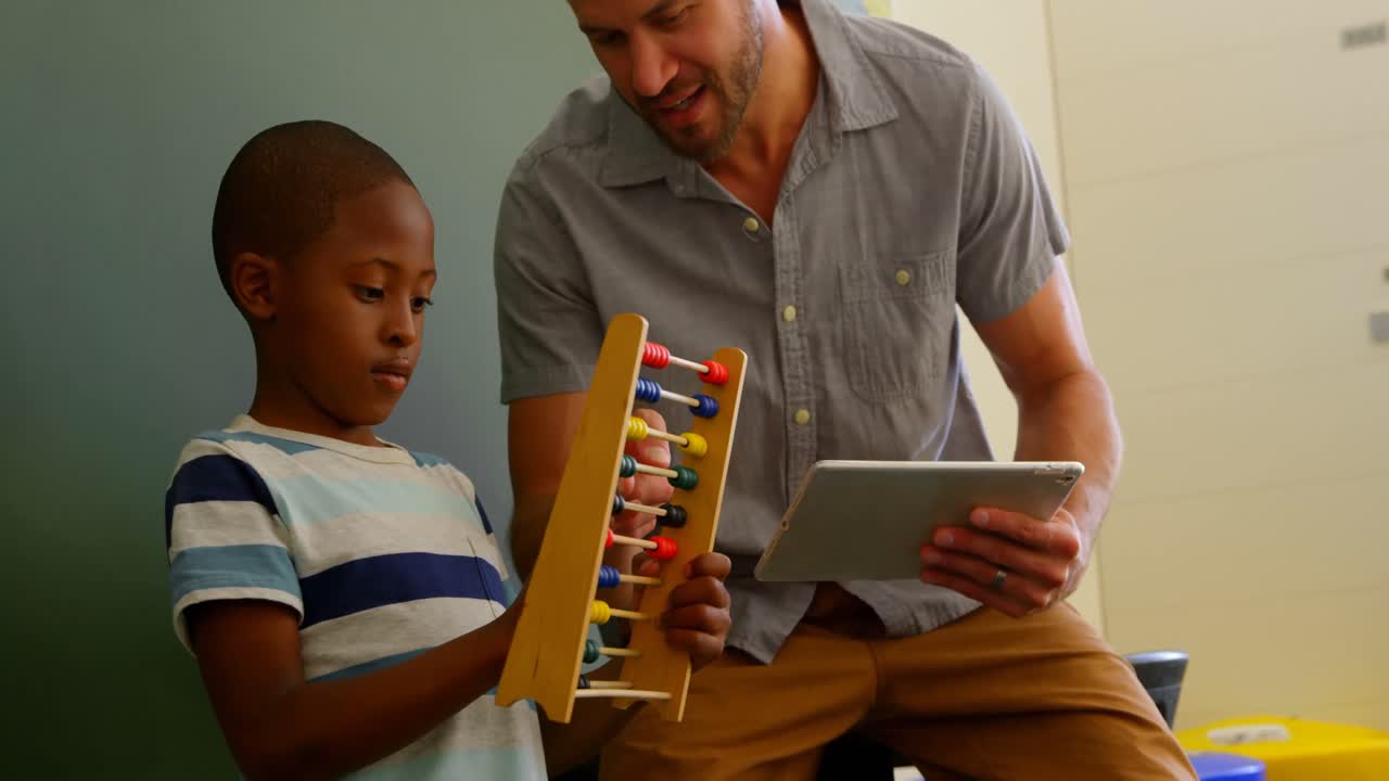 Front view of young Caucasian male teacher teaching schoolboy to use abacus in classroom 4k