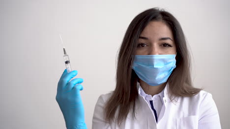 portrait of female doctor wearing medical mask and gloves holding a syringe with a vaccine for covid 19