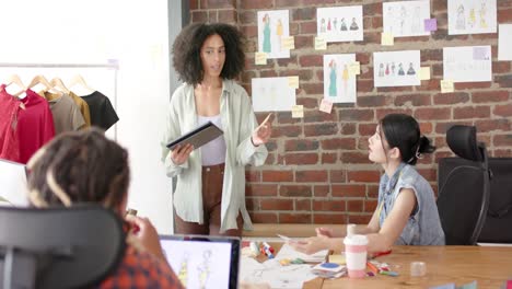 diversos diseñadores ocupados usando tablets y computadoras portátiles discutiendo en un estudio de diseño de moda en cámara lenta