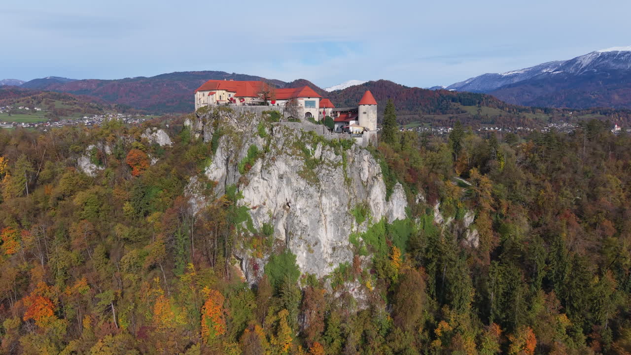 Aerial view of the medieval Bled Castle on a cliff surrounded by autumn forest in Slovenia