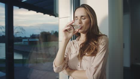 Relaxed-woman-drinking-water-near-panoramic-window.-Thirsty-lady-drinking-water