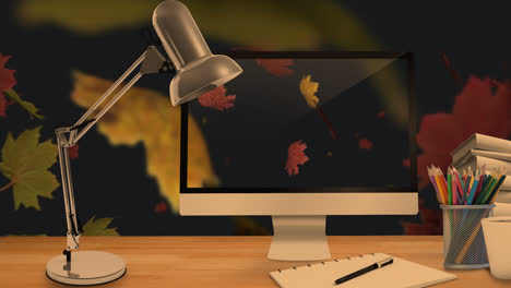 desktop computer and office equipment on a table against autumn maples leaves floating in background