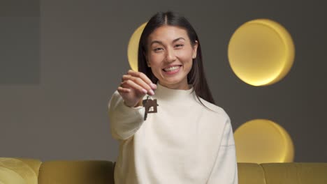 portrait of a smiling asian female tenant showing the keys to a new apartment, looking into the camera, a happy customer excited about buying a new house